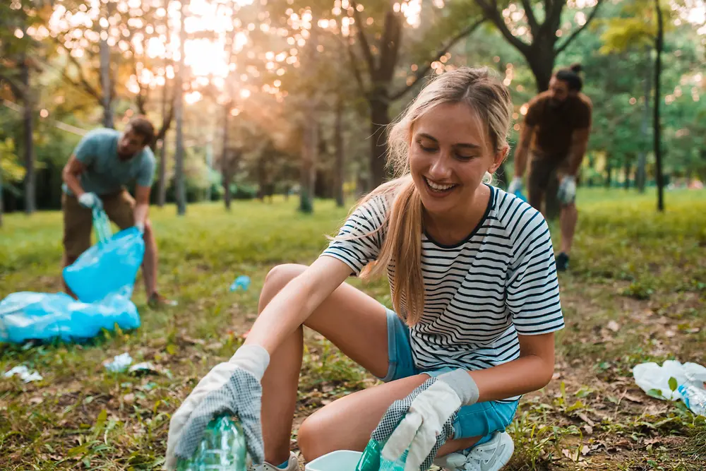 Eine Frau und zwei Männer sammeln Plastikmüll in der Natur