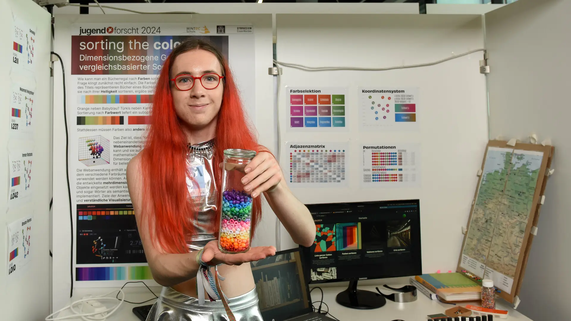 Leo Blume steht vor ihrem mit vielen Dokumenten versehenen Projektstand und hält ihr Projektmaterial in die Kamera.