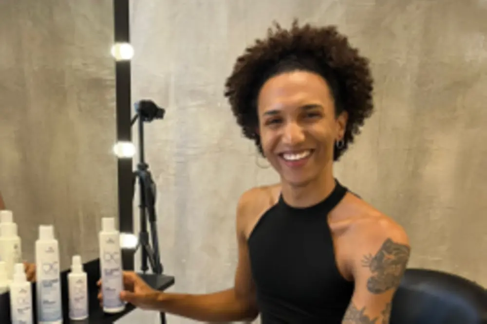Guina sitzt auf einem Stuhl im Friseursalon und lacht in die Kamera.