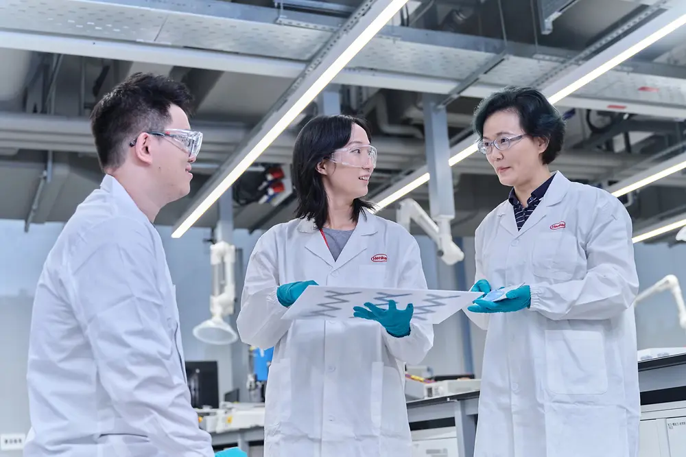 Zwei Wissenschaftlerinnen und ein Wissenschaftler beim Austausch in einem Labor.